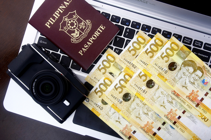 A camera, Philippine passport and several 500 Philippine peso bills on a laptop keyboard.