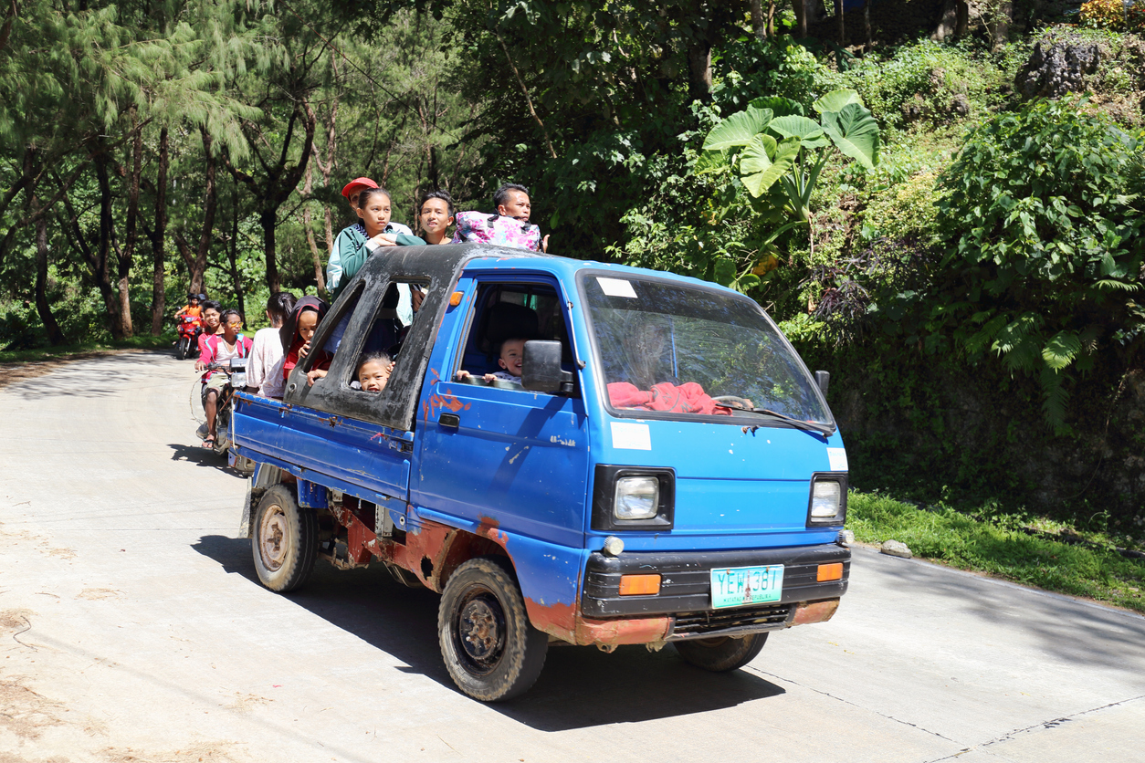 Several people riding a small blue truck in the mountains.