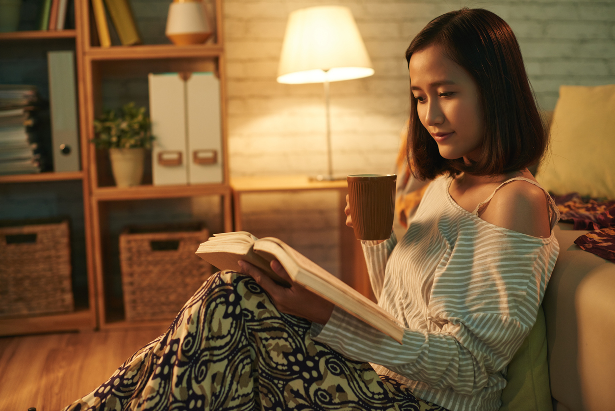 A girl sat on a couch while reading a book.