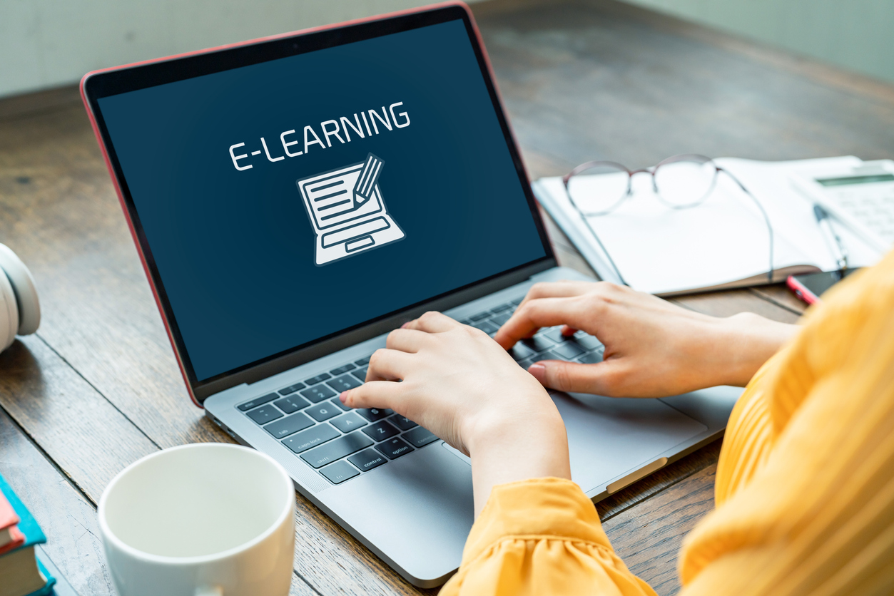 A lady's hands typing on a laptop with screen showing e-learning