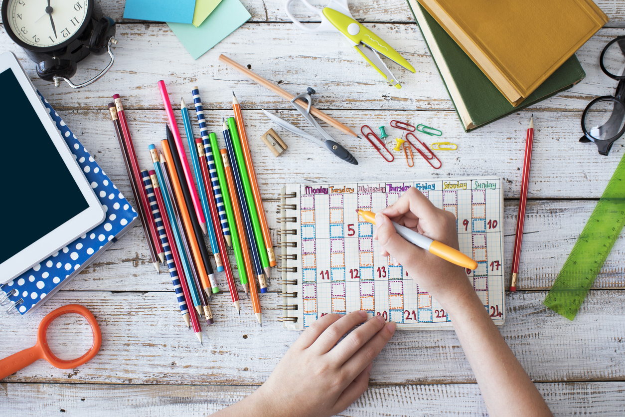 Two hands creating a study plan on a table full of stationery.